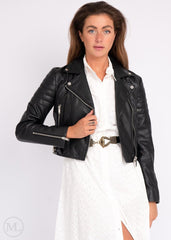 Woman wearing a black leather  biker jacket over a white outfit on a plain background