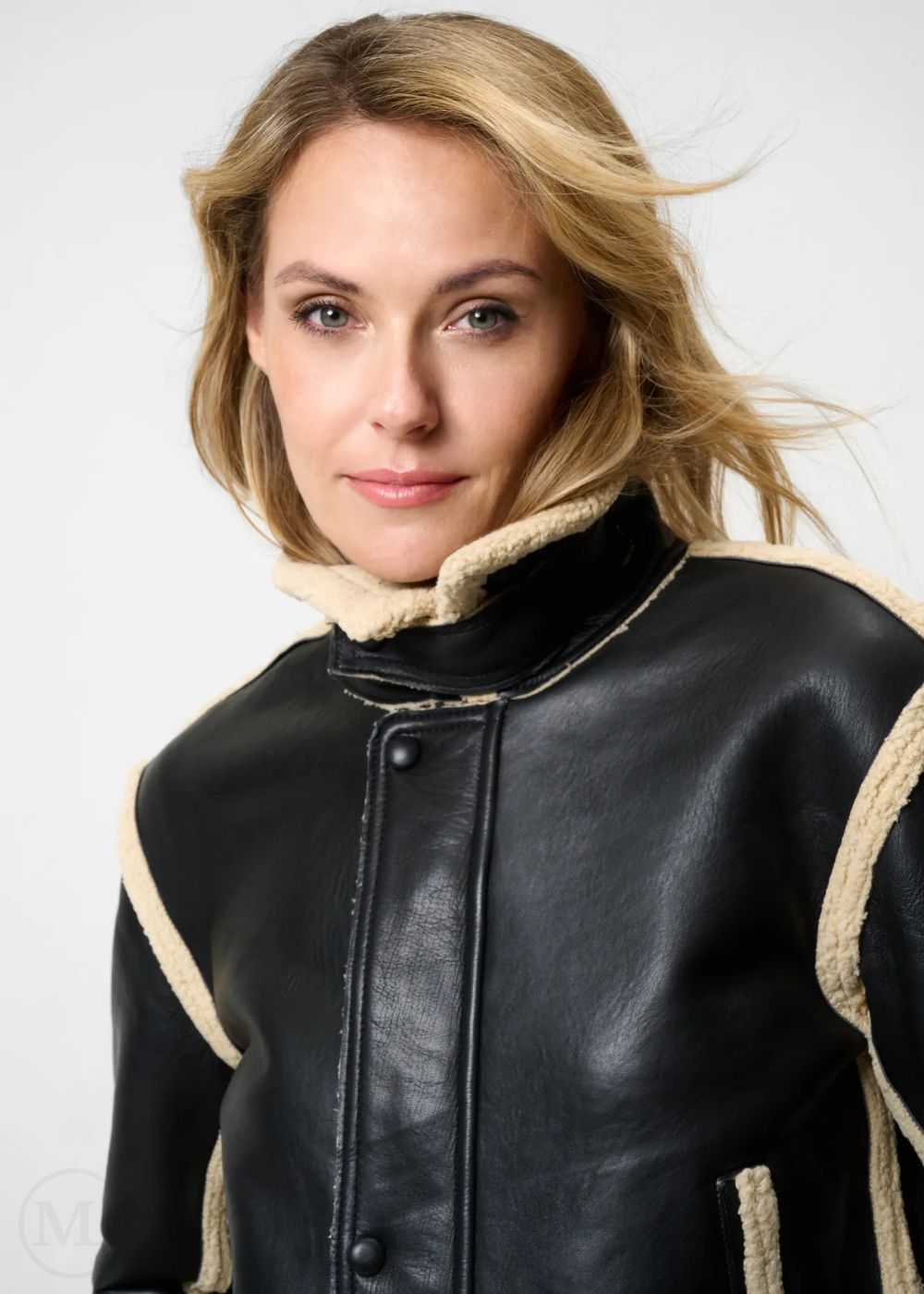 Woman wearing a black leather aviator jacket with beige trim on a white background