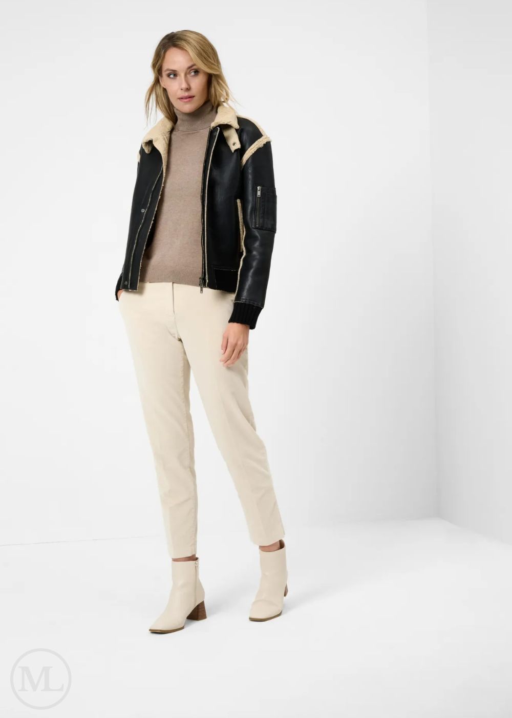 Woman wearing a black leather Aviator jacket with cream interior, beige sweater, and pants on a white background