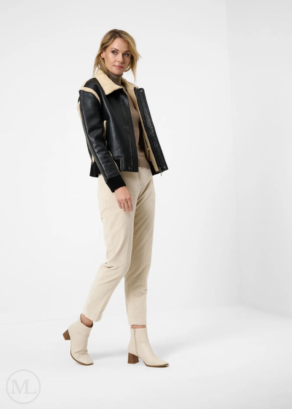 Woman wearing a black leather aviator  jacket with shearling collar, beige sweater, pants, and boots on a white background