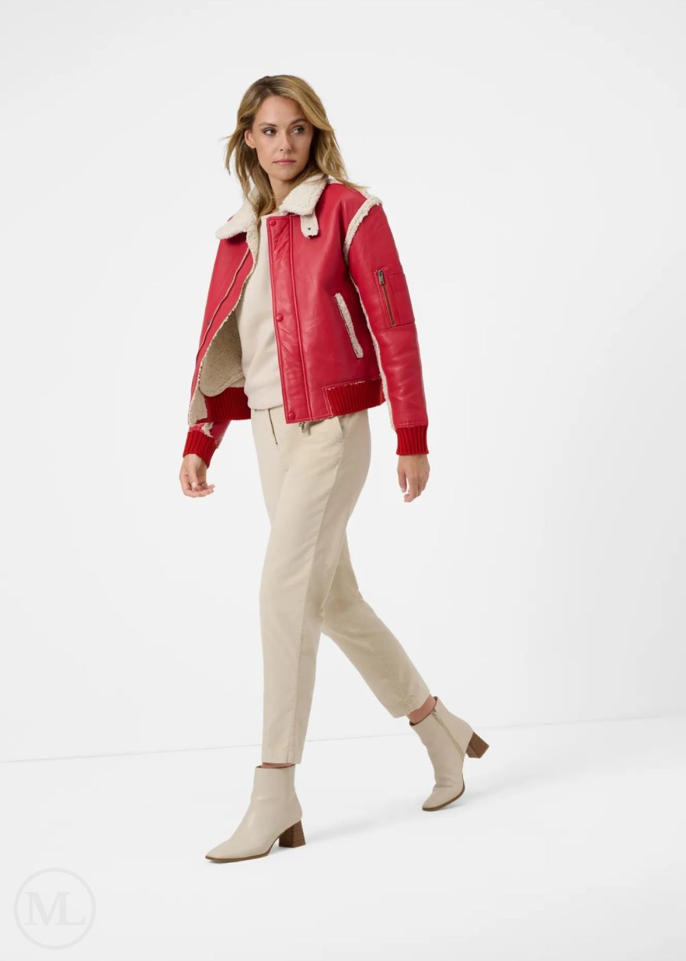 Woman wearing a leather red aviator jacket with a white collar, beige top, and pants on a white background