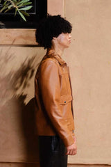 a young boy with curly hair giving side a pose while wearing a Designer men’s camel color leather trucker jacket with flap chest pockets, and welt side pockets,
