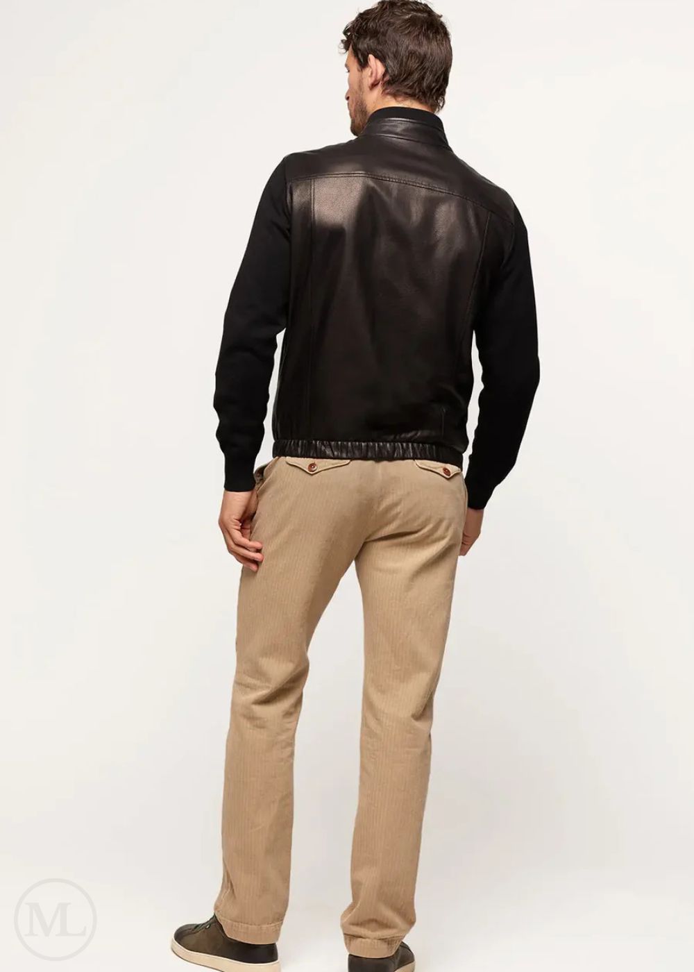 Man wearing a black leather bomber jacket and beige pants on a white background