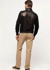 Man wearing a black leather bomber jacket and beige pants on a white background