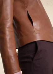 Close-up of a brown leather moto jacket and dark pants on a beige background