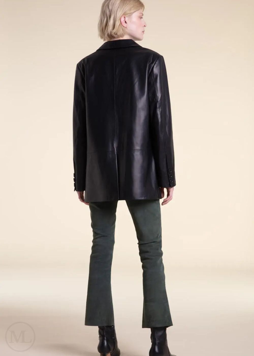 Woman wearing a black leather blazer jacket and green pants on a beige background