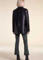 Woman wearing a black leather blazer jacket and green pants on a beige background