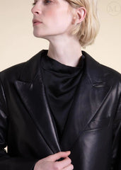 Woman wearing a black leather blazer jacket with a plain background