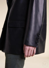 Close-up of a  woman wearing a black leather blazer jacket with buttons on a beige background