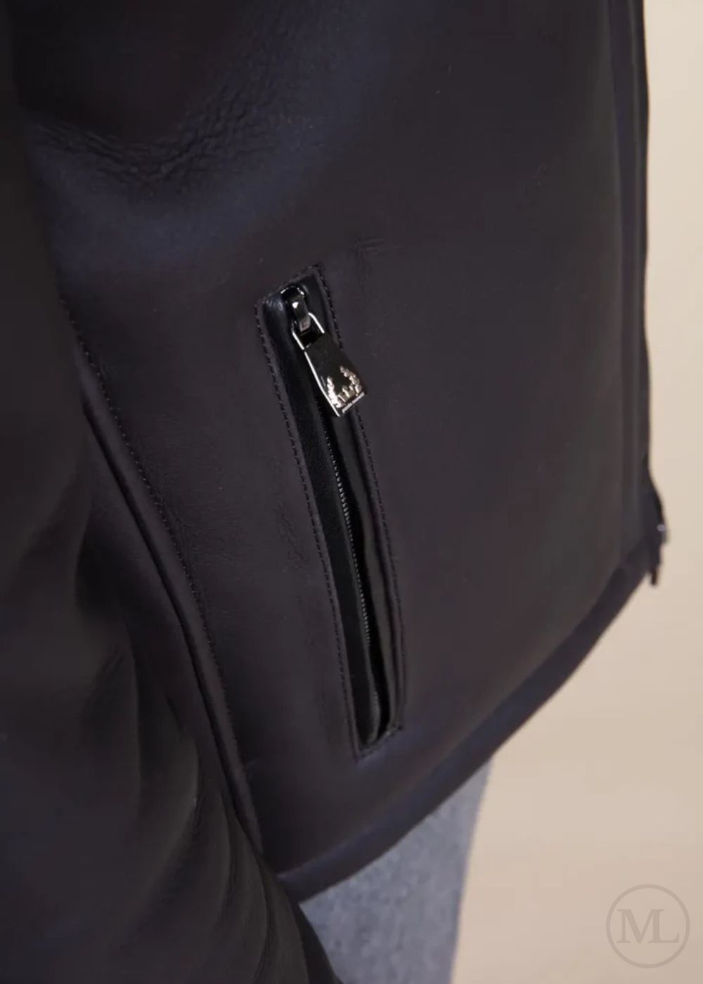 Close-up of a dark grey leather jacket with a zipper detail on a neutral background