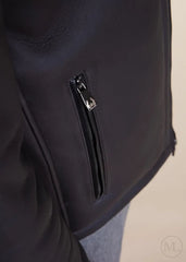 Close-up of a dark grey leather jacket with a zipper detail on a neutral background