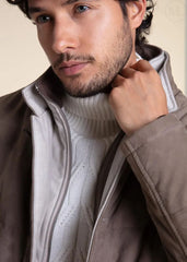 Man wearing a camel suede leather jacket over a white sweater with a neutral background