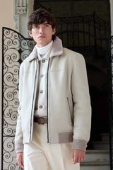 Man wearing a white shearling jacket and pants standing in front of an ornate metal gate. old money outfit