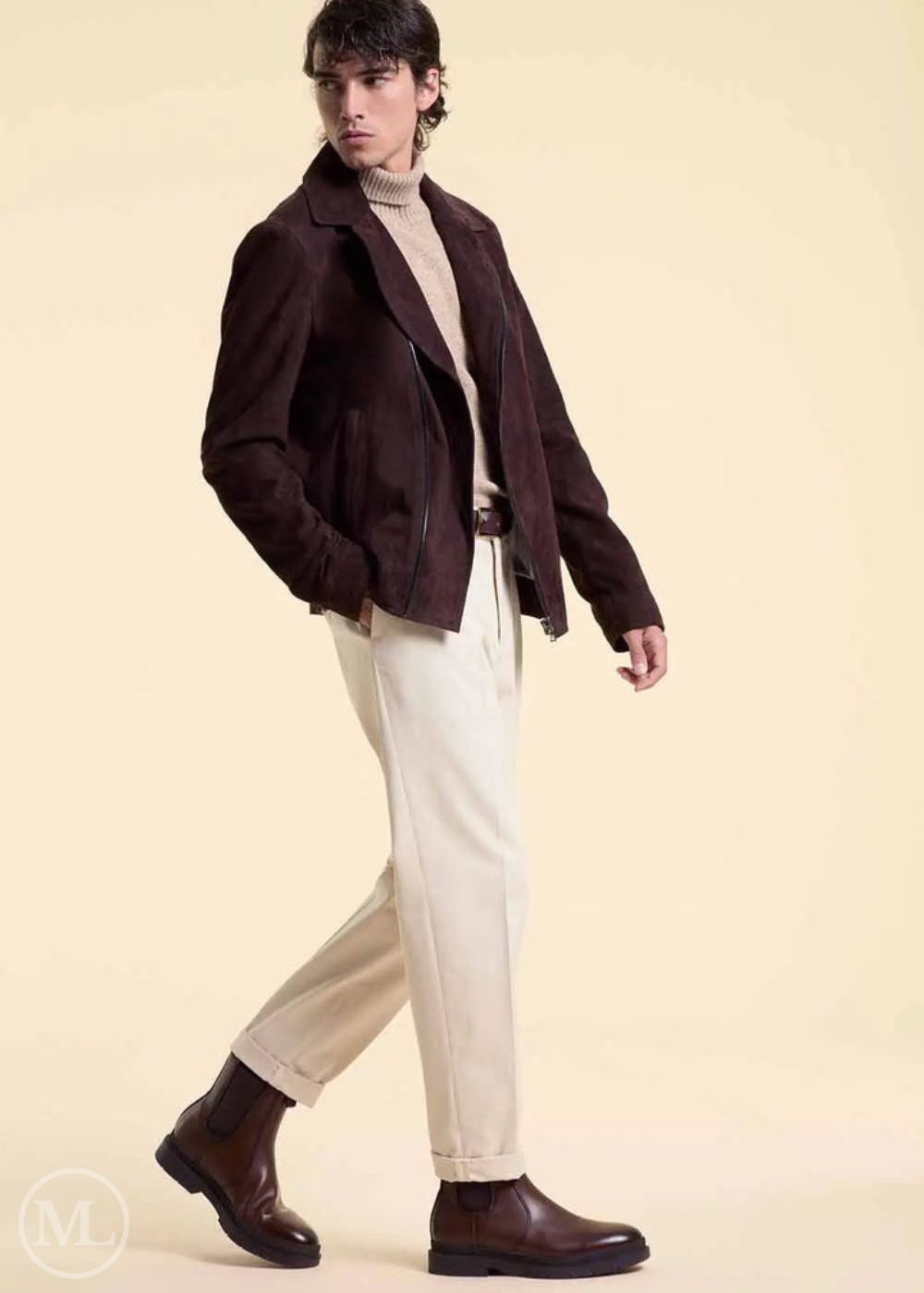Man wearing a dark brown suede jacket, beige sweater, white pants, and brown shoes on a beige background