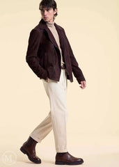 Man wearing a dark brown suede jacket, beige sweater, white pants, and brown shoes on a beige background