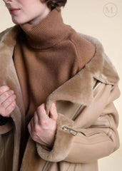 Close-up of a women wearing a shearling leather coat with fur lining on a beige background