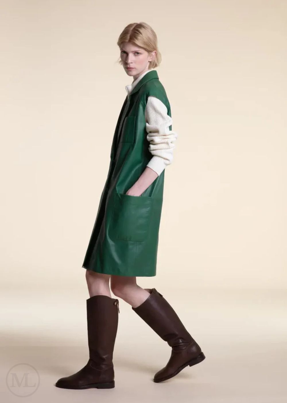 Woman wearing a Emerald green coat and brown boots on a beige background