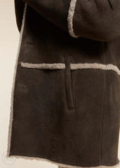Close-up of a brown suede coat with light brown trim on a beige background