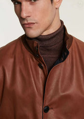 Man wearing a camel leather bomber jacket over a brown turtleneck sweater on a plain background