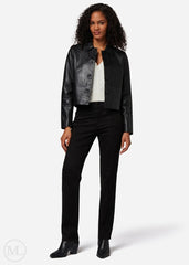 Woman wearing a black leather cropped jacket, white top, and black pants on a white background
