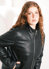 Women wearing a black leather down jacket against a plain background, leaning foward