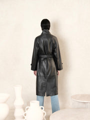 women standing backward wearing black leather trench coat with belted waist and a beige background and back view of coat