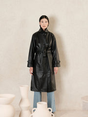 women wearing a black leather trench coat with belted waist and a beige background