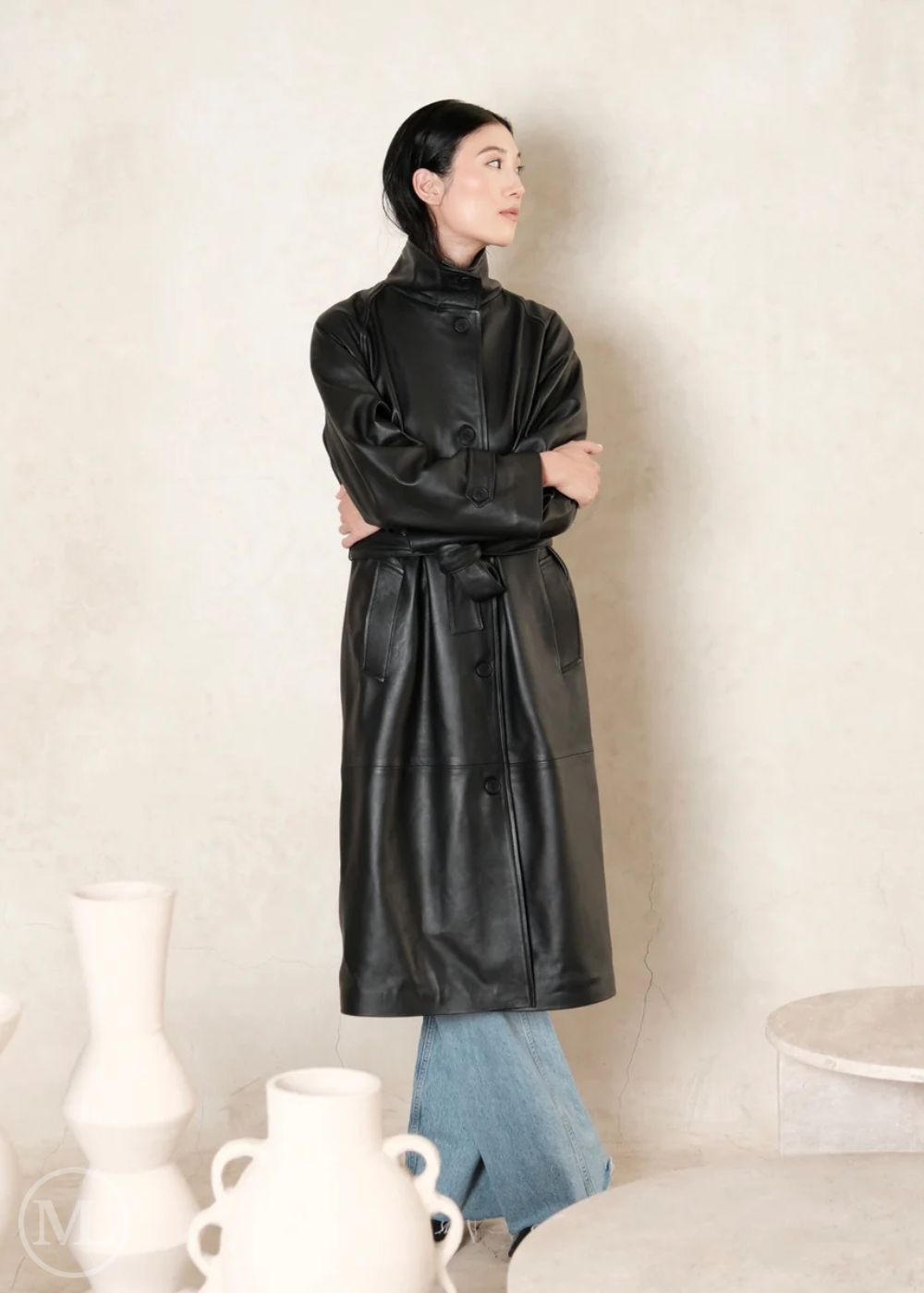 women wearing a black leather trench coat in a minimal beige wall  indoor 