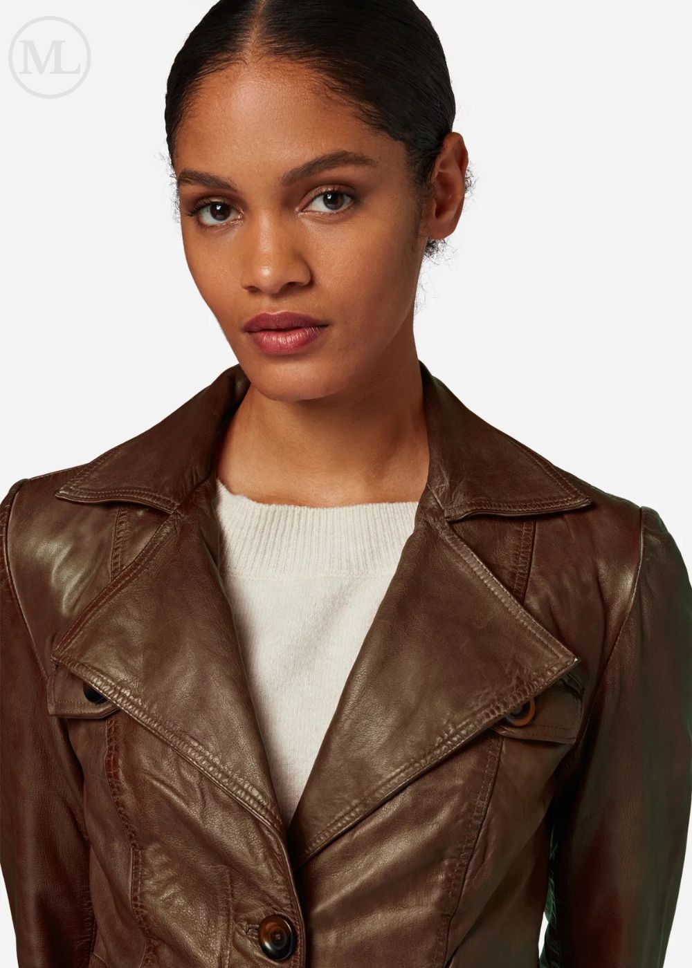 Woman wearing a brown leather coat over a white sweater on a light gray background