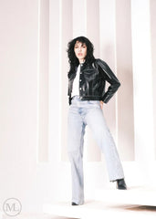 Women wearing a Cropped black leather Trucker jacket and light blue jeans against a neutral background