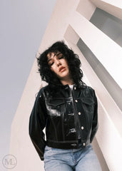 Women wearing a Cropped black leather Trucker jacket and light blue jeans against a neutral background