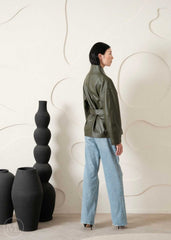 Women wearing a green jacket and blue jeans standing next to black vases against a white wall.