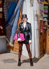 Women wearing a black leather blazer coat outfit with a pink clutch in an urban setting