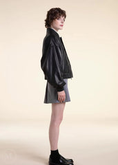Woman wearing a black leather bomber jacket and gray skirt on a beige background