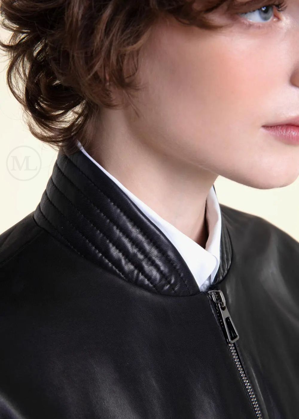 Close-up of a woman wearing a black leather bomber jacket with a neutral background