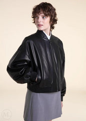 Woman wearing a black leather bomber jacket and gray skirt on a beige background
