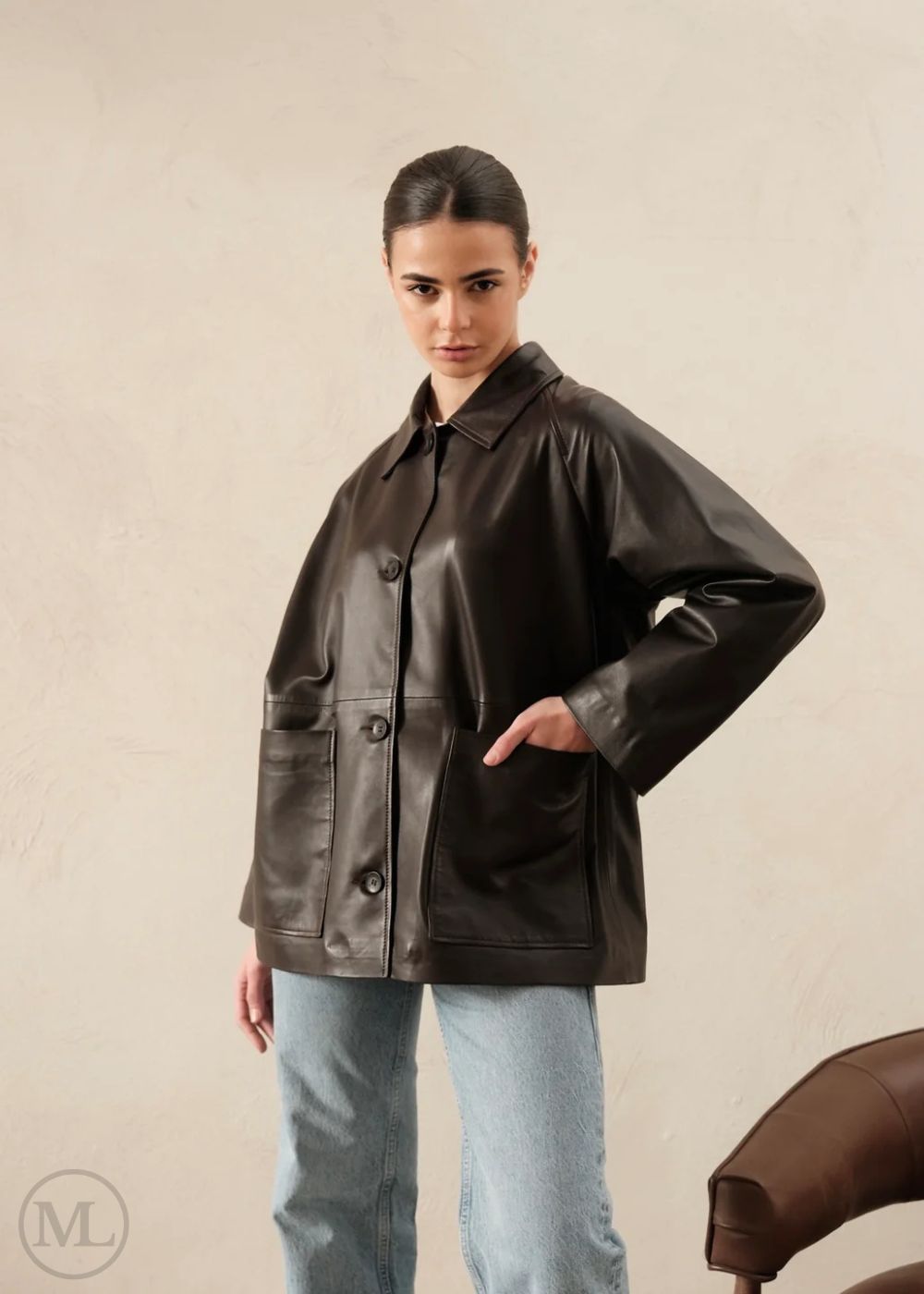 Woman wearing a dark brown leather trucker jacket against a beige background