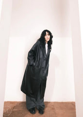 Women wearing a  Long Leather Trench Coat standing in a minimalist setting with white columns.