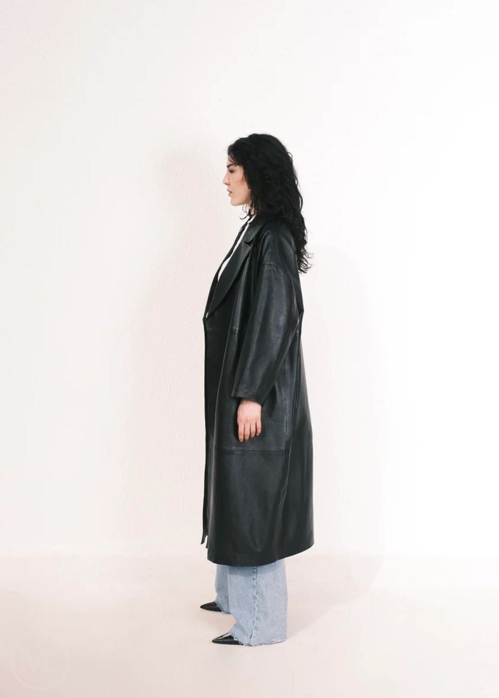 Women wearing a  Long Leather Trench Coat standing in a minimalist setting with white columns.