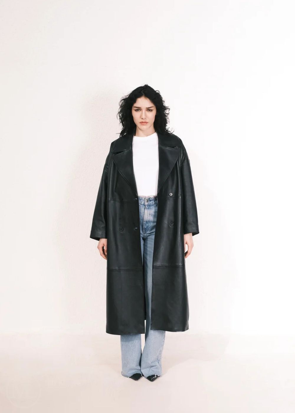 Women wearing a  Long Leather Trench Coat standing in a minimalist setting with white columns.