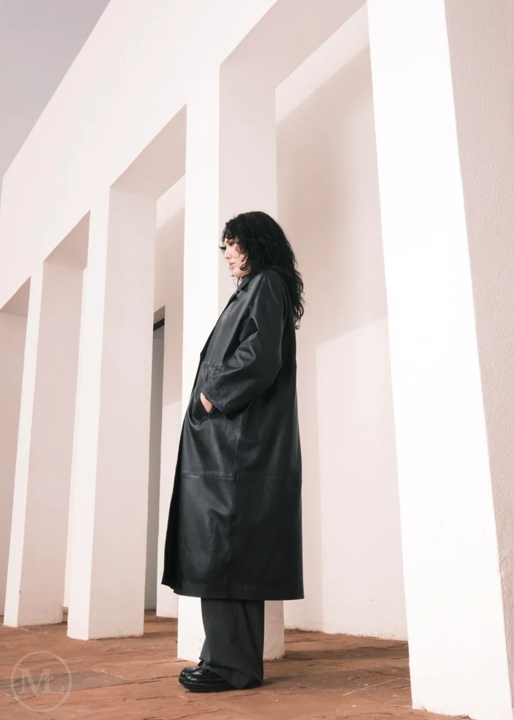Women wearing a  Long Leather Trench Coat standing in a minimalist setting with white columns.