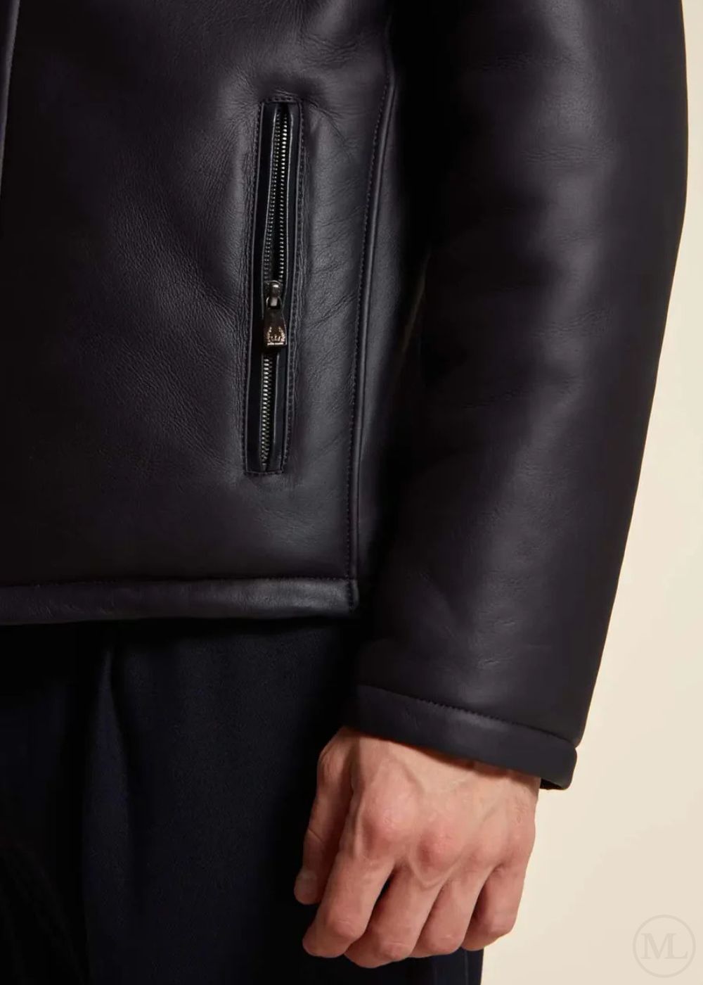 Close-up of a dark blue leather jacket with a zipper worn by a man on a beige background