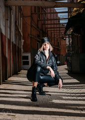 Women in black outfit and hat sitting on a brick path with industrial background