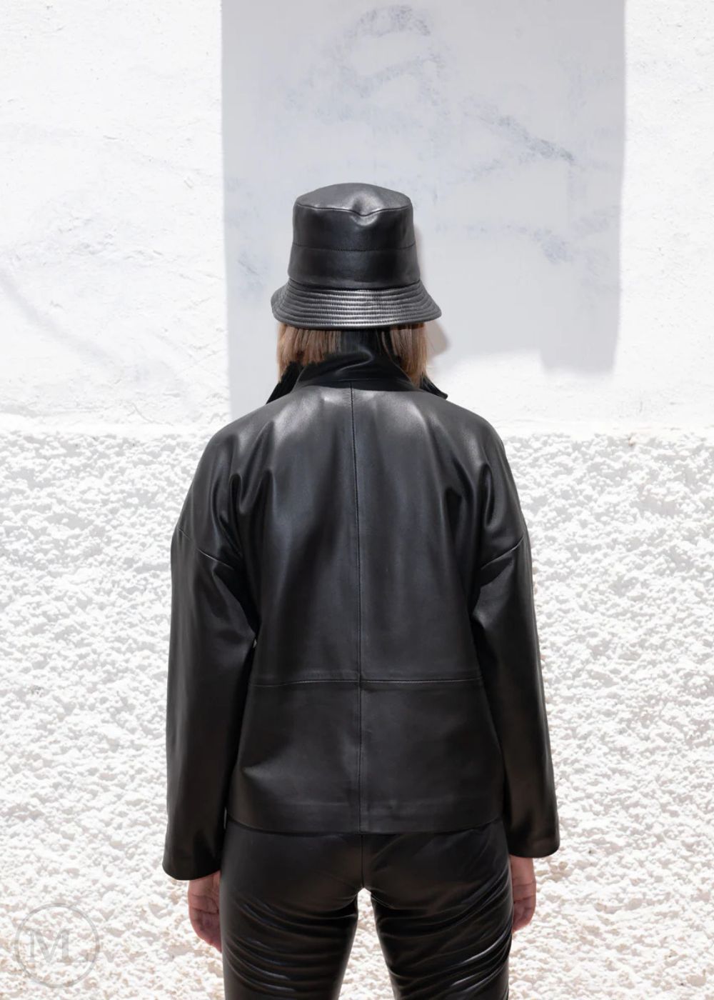 Women wearing a black leather jacket and pants with a matching hat against a textured white background