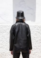 Women wearing a black leather jacket and pants with a matching hat against a textured white background