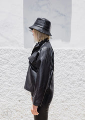 Women wearing a black leather jacket and hat against a textured white wall.
