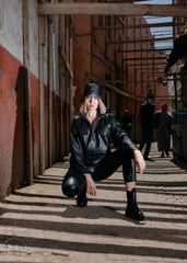 Person in black leather jacket posing in an alleyway with warm-toned walls.