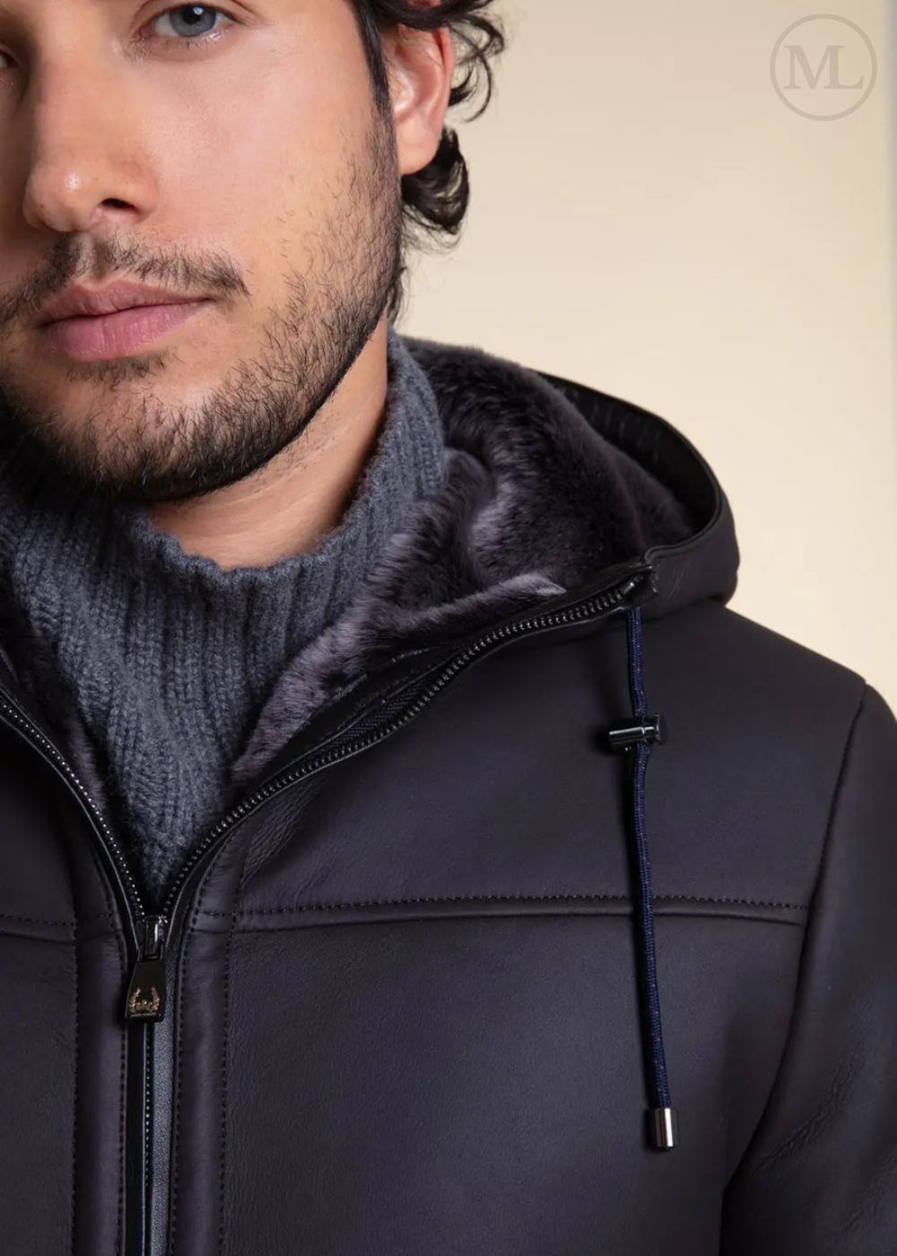 Man wearing a dark Grey Hooded Shearling jacket with a fur-lined hood against a beige background
