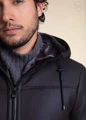 Man wearing a dark Grey Hooded Shearling jacket with a fur-lined hood against a beige background