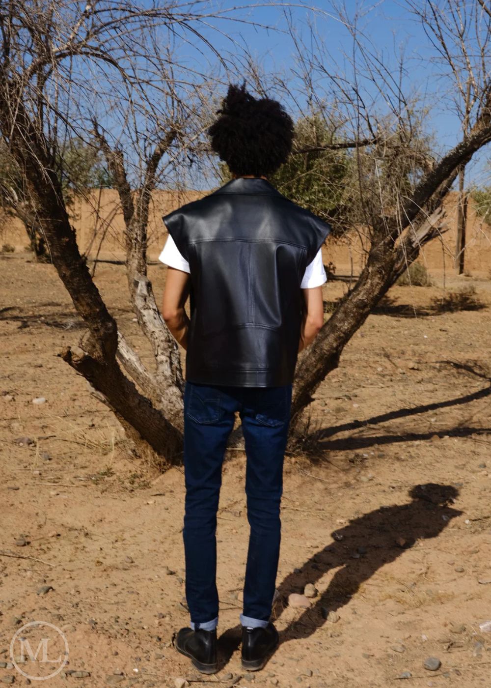 Men wearing a black leather vest standing in a dry, treeless landscape.